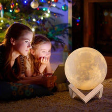 Load image into Gallery viewer, Two children looking at a moon lamp in a cozy room with a decorated Christmas tree.