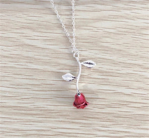 Close-up of a silver and gold necklace featuring a detailed red rose pendant, styled for women.